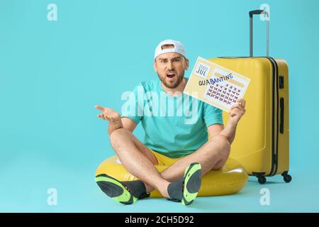 Angry man holding calendar with written word QUARANTINE against color background. Vacation concept Stock Photo