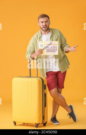 Angry man holding calendar with written word QUARANTINE against color background. Vacation concept Stock Photo