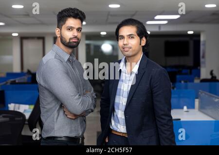 Portrait of two young handsome Indian businessmen standing against office background, corporate environment. Stock Photo