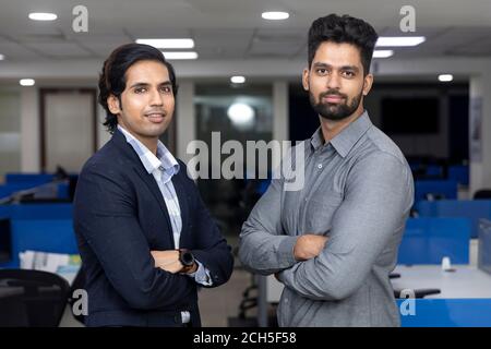 Portrait of two young handsome Indian businessmen standing against office background, corporate environment. Stock Photo