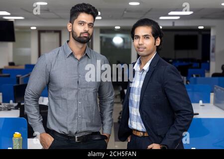 Portrait of two young handsome Indian businessmen standing against office background, corporate environment. Stock Photo