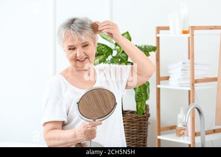 Senior woman combing her hair at home Stock Photo