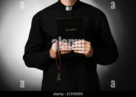 Handsome priest with Bible on dark background Stock Photo