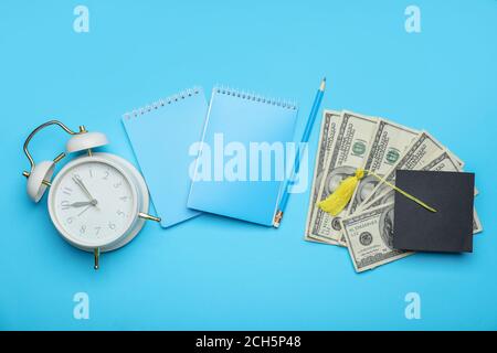 Graduation hat, money, notebooks and alarm clock on color background. Tuition fees concept Stock Photo