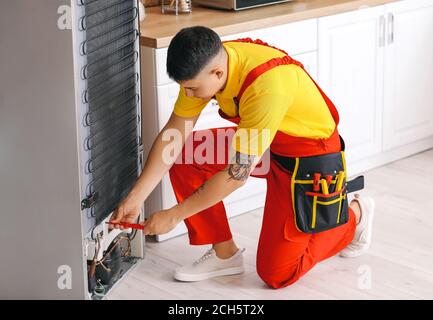 Worker repairing fridge in kitchen Stock Photo