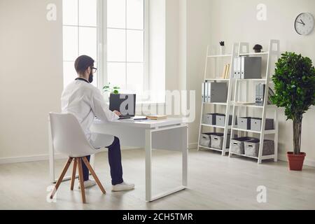 Doctor online consultation. Male therapist uses laptop video chat for consultation sitting at the table in the office of the clinic. Stock Photo
