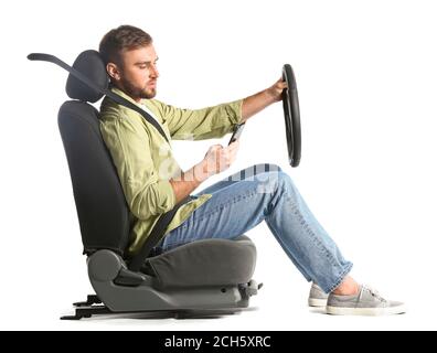Young man with steering wheel and mobile phone sitting on car seat against white background Stock Photo