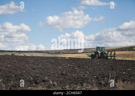 Tractor plowing black soil field with blue sky and white clouds Stock Photo