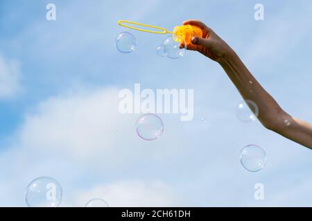 childs hand holding a wand for blowing soap bubbles against the blue sky on a sunny summer day Stock Photo