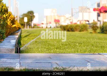 Automatic irrigation system irrigated the lawn on a blurred background of the cityscape on a bright sunny day, copy space. Stock Photo