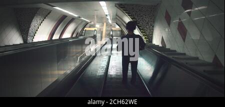 Silhouette of young man listening to music with headphone standing on escalator going downwards inside the subway Stock Photo