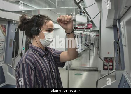 Masked long haired thoughtful millennial young adult listening to music from his headphone holding a handle inside the subway Stock Photo
