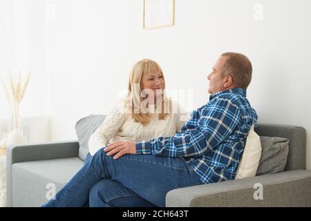 Happy meddle age couple at home. Handsome mature man and attractive woman talking and enjoying spending time together while sitting on sofa. Stock Photo