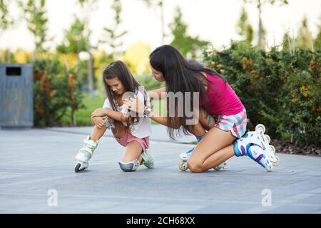 little child girl falled down while rolling with her mother in park. mom helps daughter get up after falling Stock Photo