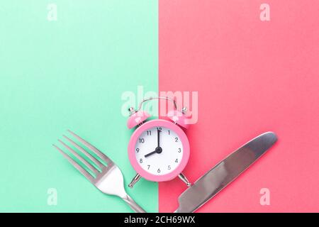 Pink alarm clock, fork, knife on colored paper background. Intermittent fasting concept - Image Stock Photo