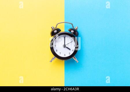 Black alarm clock on two tone color yellow and blue background. Top view, place for text - Image Stock Photo