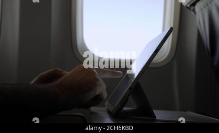 Male hands using modern digital tablet at airplane. Stock Photo