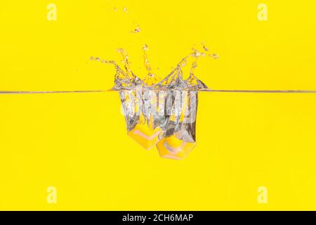 Falling of ice cubes into water on color background Stock Photo