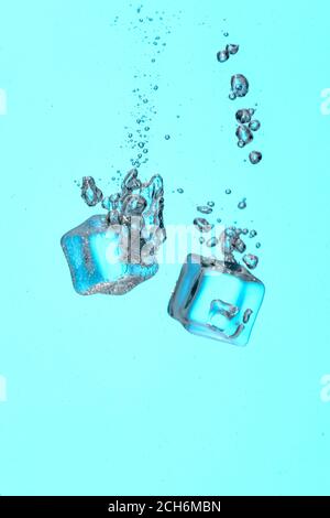 Falling of ice cubes into water on color background Stock Photo