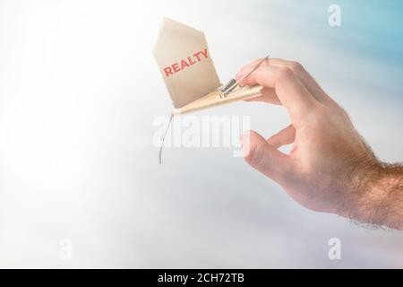 Bank investments and risks. A man's hand was caught in a mousetrap with a schematic cardboard house, with the inscription REALTY. In the background, h Stock Photo