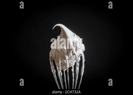 Metal whisk with whipped egg whites, isolated on black background, close up Stock Photo