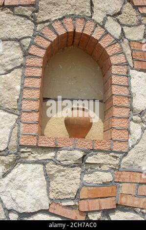 Antique clay jar in wall arch with stones and bricks Stock Photo