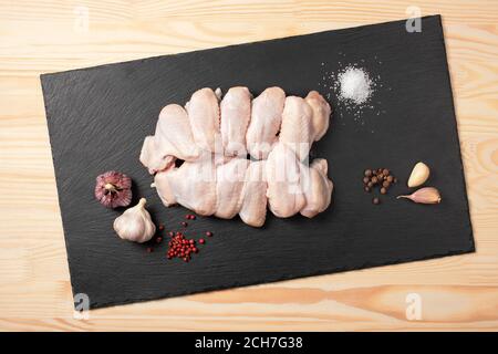 Raw chicken wings. Fresh chicken wings with spices on cutting board. Raw chicken wings with ingredients for cooking on a slate cutting board over wood Stock Photo