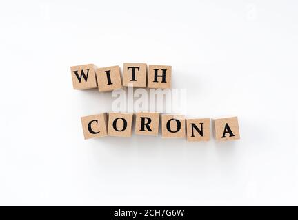 A wooden block with the word "with corona" written on it on a white background Stock Photo