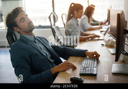 Young tired, ill, overworked business man in formal wear sitting in front of computer Stock Photo