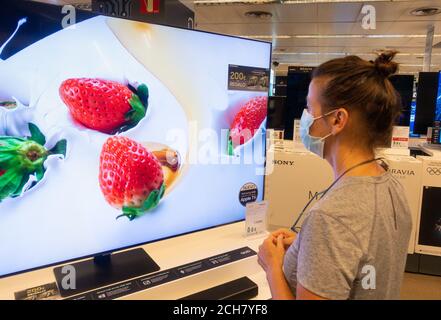 Woman wearing face mask looking at high definition television, TV screen in store.