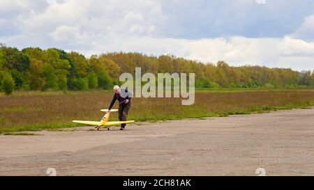 An elderly man launches a radio-controlled aircraft on the runway in the spring. Stock Photo