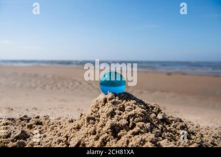 Blue glass ball on sand near the sea. Abstract conceptual photo. Stock Photo