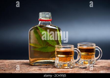 Alcoholic drink like whiskey brandy or schnapps infused with cannabis leaves in the bottle on the table with dark copy space Stock Photo