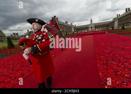 Chelsea Pensioner piper Michael Shanahan, 70, playing at the 5000 Poppies exhibit - which uses almost 300,000 individually crocheted poppies, covering nearly 2,000sq m (21,000sq ft) in the grounds of the Royal Hospital Chelsea - during a preview day at the Chelsea Flower Show in London. Stock Photo