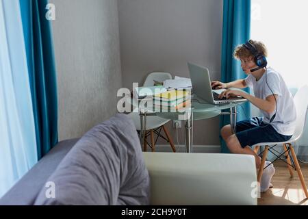 lazy teenager boy play computer games, sit in headphones, looking at screen  of laptop, free time at home Stock Photo