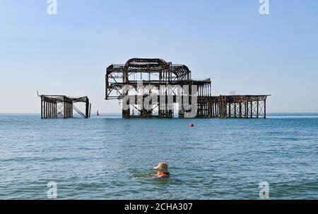 Brighton UK 14th September 2020 - A swimmer keeps her hat on as she enjoys the hot sunny weather in Brighton by the West Pier as temperatures are forecast to reach 30 degrees in parts of the South East  : Credit Simon Dack / Alamy Live News Stock Photo