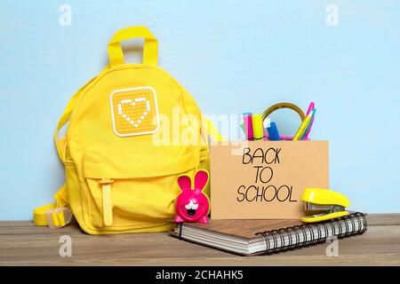 Back to school composition, education concept. Yellow backpack with school supplies - notebook, pens, stapler, pencil, sharpener isolated on blue Stock Photo