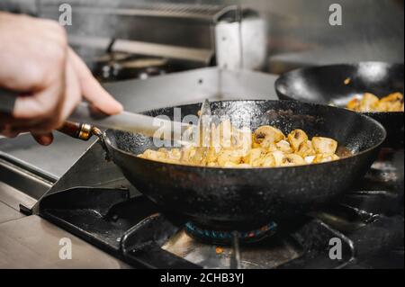 Chef cooking mushrooms in frying pan on burning fire. High quality image. Stock Photo
