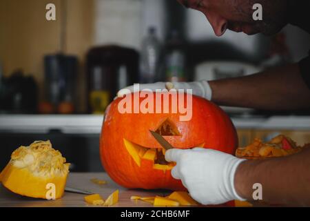 Man making Halloween pumpkin head jack lantern on wooden table at home, closeup. Stock Photo