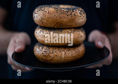 A men's hands holding a plate full of Bagels on a Black Background Stock Photo