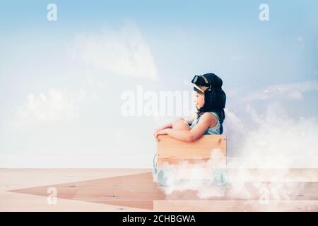 happy kid girl racing fast to her future in a wood car box - life dreams and personal growth concept Stock Photo