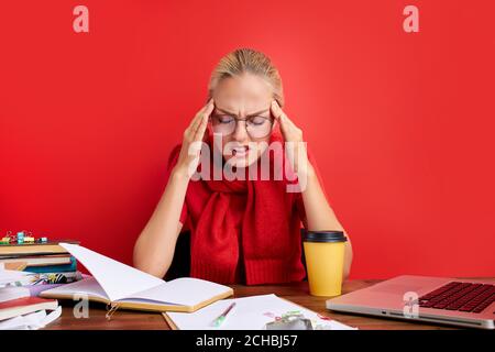 woman has head burst at work, she is suffering from head ache, sit with paper at office desk Stock Photo