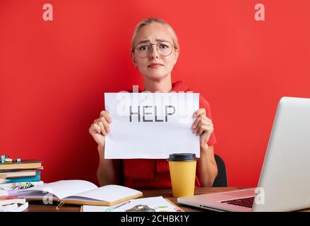overworked unhappy and frustrated young caucasian woman in stress sitting at office desk, she has a lot of tasks in work, deadline, isolated red backg Stock Photo