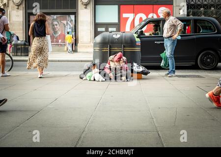 London- September, 2020: A homeless man sits slumped as shoppers walk by on Oxford Street Stock Photo