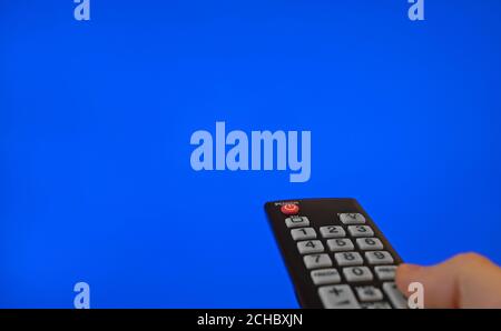 Male hand with remote control pointing on TV screen. Blue chroma key. Stock Photo