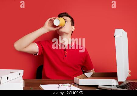 good-looking male drink coffee at work place, sits in the office. isolated red background Stock Photo