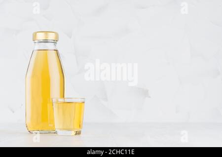 Fresh yellow transperent apple juice in glass bottle mock up with wine glass on white wood table in light interior, template for packaging, advertisin Stock Photo