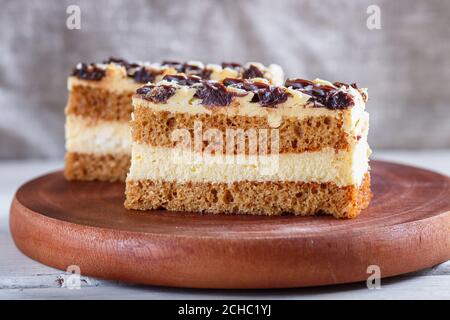 a piece of cake with milk and butter  cream on a wooden kitchen board, close up, selective focus, white background. Stock Photo