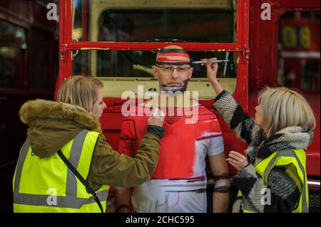 Mark Ellis, who survived open heart surgery 50 years ago, is painted red by make-up artist Carolyn Roper (right) and her assistant Scarlett Jones to blend into a Routemaster bus to launch the British Heart Foundation's (BHF) 'Wear it. Beat it.' campaign in Purfleet. Stock Photo