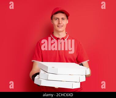 man in red uniform with fast food order isolated on red background, male courier holding pizza for clients, wearing protective gloves Stock Photo